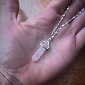 May include: A silver chain necklace with a clear quartz crystal pendant. The crystal is shaped like a point and is set in a silver bezel.
