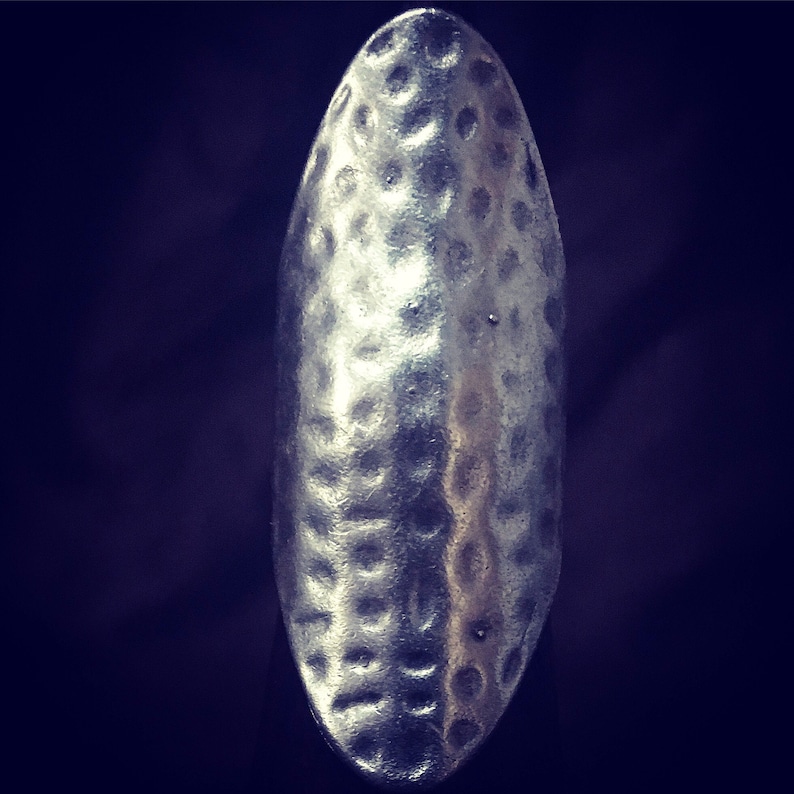 May include: A silver ring with a hammered texture. The ring is oval shaped and has a smooth, polished finish.