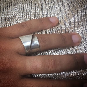 Può includere: Un anello d'argento con un designo unico e attorcigliato. L'anello è indossato su un dito.