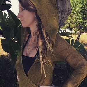 May include: A brown hooded wrap with long sleeves. The wrap is made of a textured fabric and has a loose fit. The model is wearing the wrap over a black tank top.