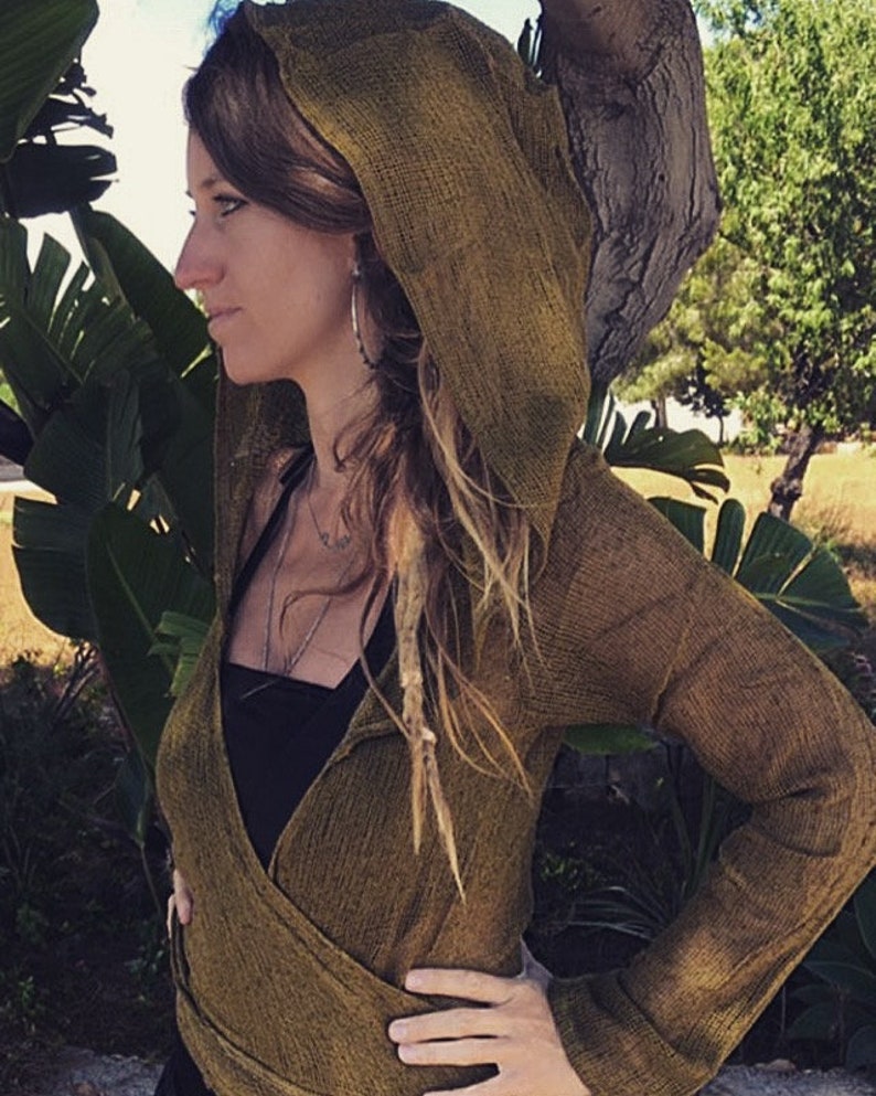 May include: A brown hooded wrap with long sleeves. The wrap is made of a textured fabric and has a loose fit. The model is wearing the wrap over a black tank top.