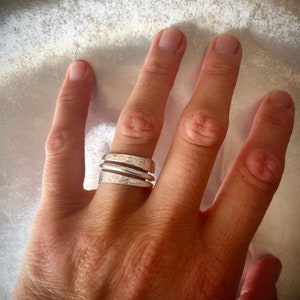 Può includere: Un anello d'argento con una texture martellata e tre bande. L'anello è indossato su un dito.