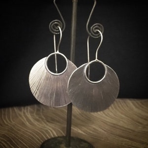 Può includere: Un paio di orecchini d'argento con un design a forma di ventaglio. Gli orecchini sono appesi a un gancio d'argento.