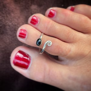 Puede incluir: Anillo de dedo del pie de plata con una piedra ovalada negra y un diseño de espiral.