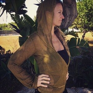 May include: A woman wearing a long-sleeved, olive green, crocheted wrap top with a hood. The top is open in the front and has a V-neckline. The woman is wearing a black tank top underneath.