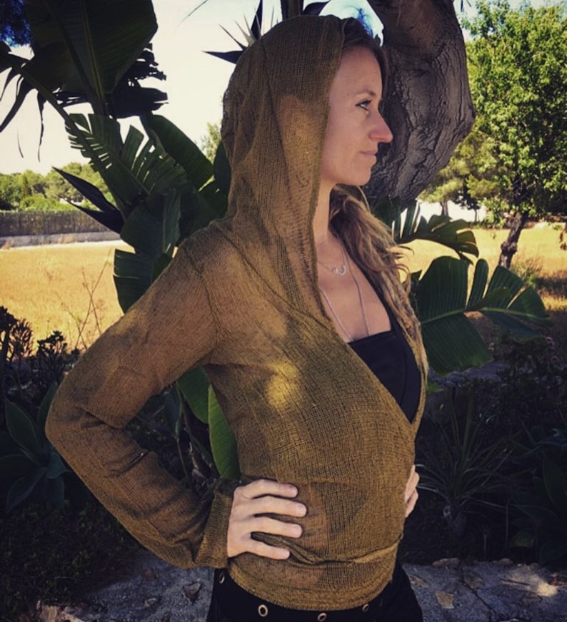 May include: A woman wearing a long-sleeved, olive green, crocheted wrap top with a hood. The top is open in the front and has a V-neckline. The woman is wearing a black tank top underneath.