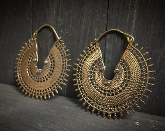 May include: A pair of large, gold-toned hoop earrings with intricate, circular designs. The earrings are made of metal and have a delicate, filigree pattern.