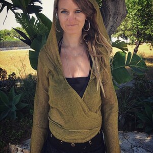May include: A green wrap top with long sleeves and a hood. The top is made of a soft, lightweight fabric and has a relaxed fit. The model is wearing the top with a black tank top underneath and a black belt.