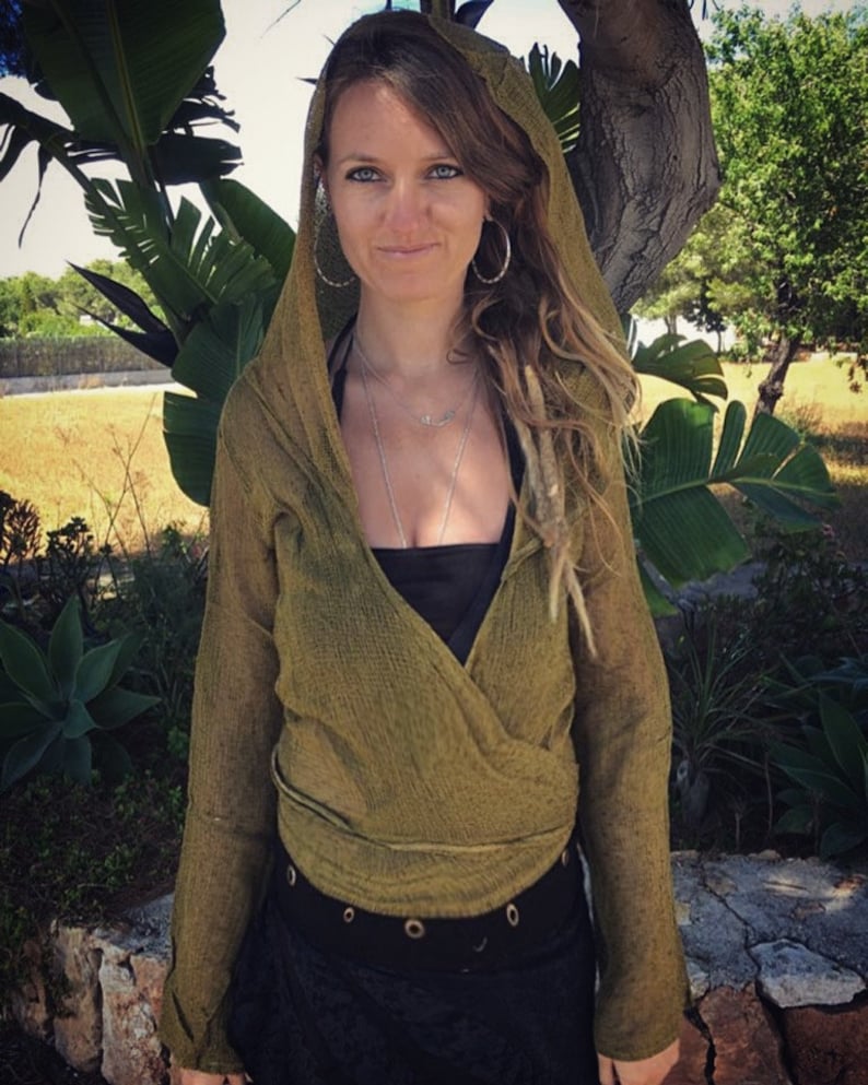 May include: A green wrap top with long sleeves and a hood. The top is made of a soft, lightweight fabric and has a relaxed fit. The model is wearing the top with a black tank top underneath and a black belt.