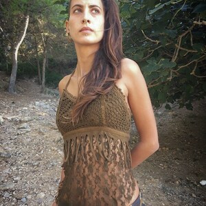 May include: A brown crochet top with fringe detailing. The top is sleeveless and has a halter neckline. The model is wearing the top with a patterned skirt.
