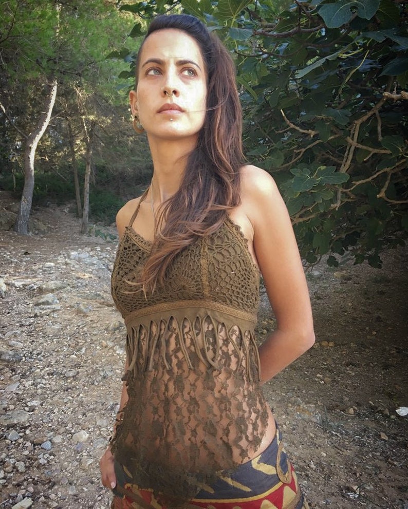 May include: A brown crochet top with fringe detailing. The top is sleeveless and has a halter neckline. The model is wearing the top with a patterned skirt.