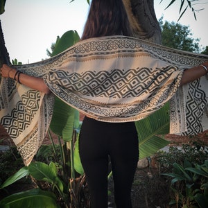Könnte beinhalten: Eine Frau trägt schwarze Leggings und einen beige-schwarzen gemusterten Schal. Der Schal hat ein geometrisches Muster mit schwarzen und weißen Rauten und einem Rand aus schwarzen und weißen Kreisen.