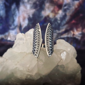 Puede incluir: Un par de anillos de plata con un diseño geométrico. Los anillos están sobre un fondo blanco.