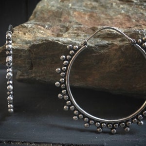 Könnte beinhalten: Ein Paar silberne Creolen mit einem Perlenmuster. Die Ohrringe sind groß und haben eine runde Form.