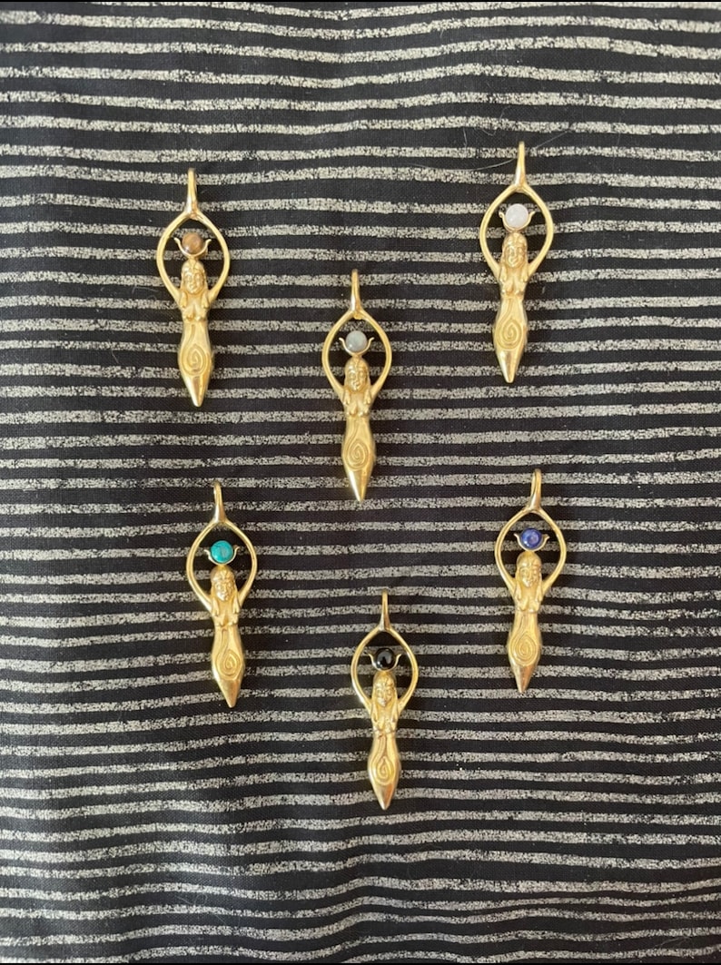 K&ouml;nnte beinhalten: Sechs goldene Anh&auml;nger mit einer weiblichen Figur, die einen Edelstein h&auml;lt. Die Edelsteine sind in verschiedenen Farben, darunter blau, gr&uuml;n, schwarz und wei&szlig;.