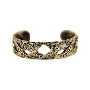 May include: A bronze cuff bracelet with an openwork design. The bracelet features two birds in flight, surrounded by branches and leaves. The metal has a slightly aged appearance, giving it a vintage feel. The bracelet is approximately 6 cm wide.