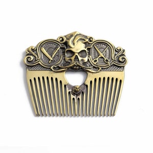 Peut inclure: Un peigne en métal doré avec un motif de crâne et d'os croisés. Le peigne a une poignée décorative avec un motif de crâne et d'os croisés. Le peigne est en métal et a une finition dorée.