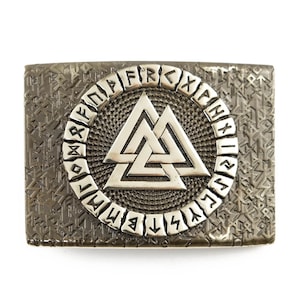 Peut inclure: Boucle de ceinture rectangulaire argent&eacute;e avec un fond textur&eacute; et un motif central. Le motif pr&eacute;sente un symbole Valknut argent&eacute; dans un cercle de runes. La boucle est probablement en m&eacute;tal.
