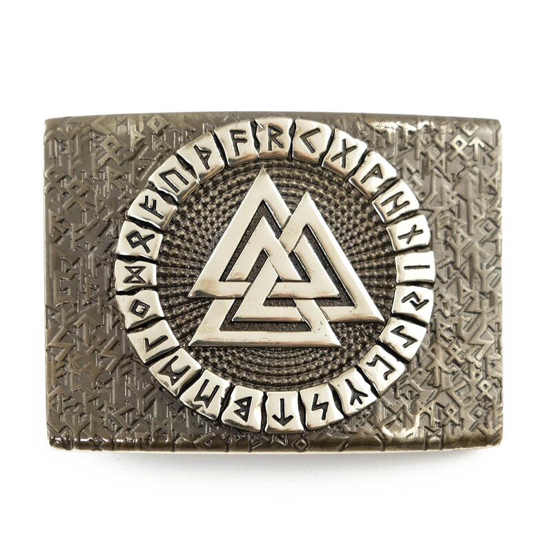 Peut inclure: Boucle de ceinture rectangulaire argent&eacute;e avec un fond textur&eacute; et un motif central. Le motif pr&eacute;sente un symbole Valknut argent&eacute; dans un cercle de runes. La boucle est probablement en m&eacute;tal.