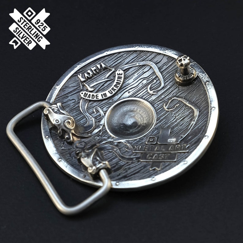 Puede incluir: Hebilla de cintur&oacute;n de plata con un dise&ntilde;o detallado de un escudo con un drag&oacute;n y el texto "Karmia Made in Ukraine Metal Art Cast".