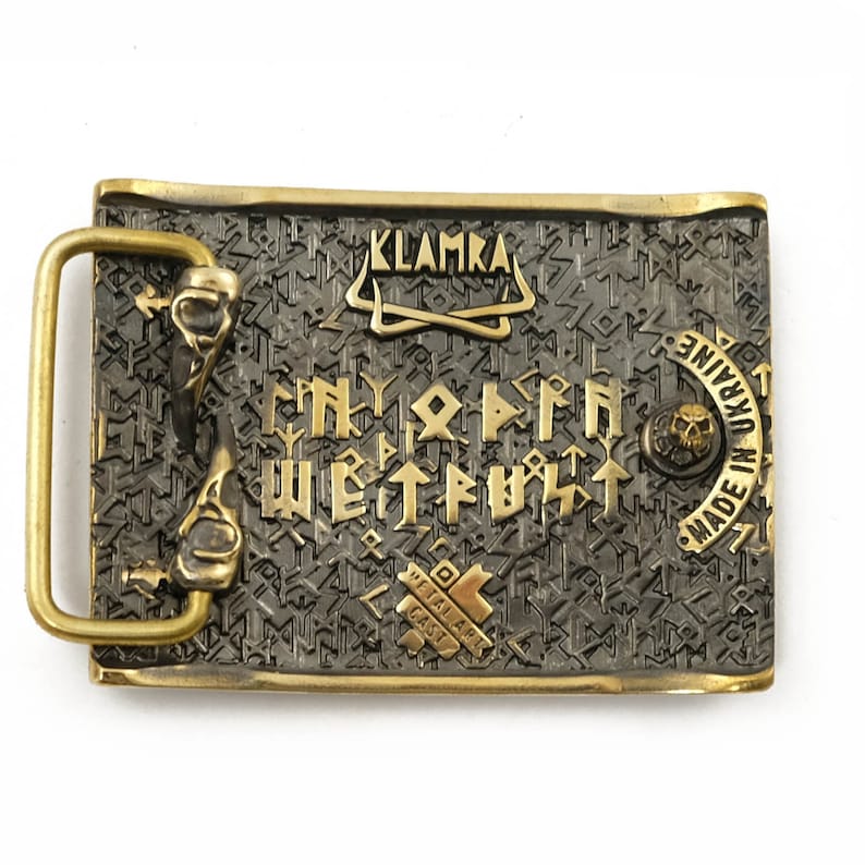 Peut inclure: Boucle de ceinture rectangulaire en m&eacute;tal avec un cadre et des accents dor&eacute;s. La boucle pr&eacute;sente un fond gris fonc&eacute; avec des lettres et des symboles dor&eacute;s. Le texte "KLAMKA" est en haut et "MADE IN UKRAINE" sur le c&ocirc;t&eacute; droit.
