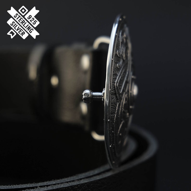 Puede incluir: Una hebilla de cintur&oacute;n de plata con un dise&ntilde;o intrincado, unida a un cintur&oacute;n de cuero negro. La hebilla est&aacute; marcada con "925 Sterling Silver".