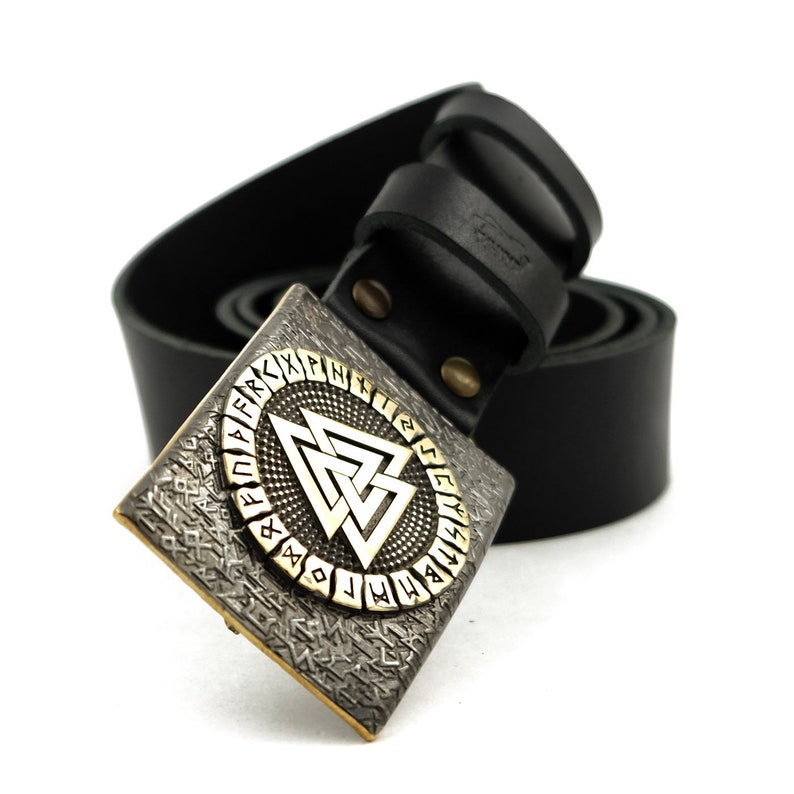 Peut inclure: Ceinture en cuir noir avec une boucle de couleur argent&eacute;e. La boucle pr&eacute;sente un motif g&eacute;om&eacute;trique avec un triangle central et des symboles runiques sur le bord. La boucle est carr&eacute;e avec un fond textur&eacute;.
