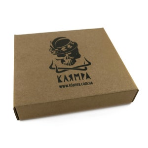 Peut inclure: Bo&icirc;te carr&eacute;e en carton brun avec un logo noir repr&eacute;sentant un cr&acirc;ne portant un chapeau et le mot "KЯAMPA" en dessous. L'adresse du site Web www.klamra.com.ua est imprim&eacute;e en dessous. La bo&icirc;te est ferm&eacute;e et pos&eacute;e sur fond blanc.
