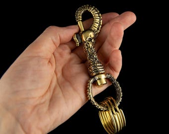 May include: A brass key chain with a skull and rose design. The chain has a large, ornate hook and multiple smaller rings.