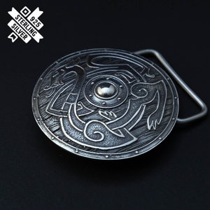 Puede incluir: Una hebilla de cintur&oacute;n de plata con un dise&ntilde;o circular que presenta un escudo con un motivo de drag&oacute;n. La hebilla est&aacute; hecha de plata de ley y tiene un sello de 925.