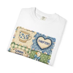 May include: White t-shirt featuring a patchwork design with a teacup, heart with "THRIFTERS" text, and a duck with a blue bow. The design includes floral and gingham patterns. The shirt is made of a soft, comfortable material.