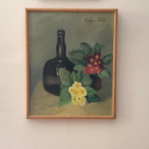 May include: A framed painting of a still life featuring a dark brown glass bottle and a bouquet of yellow and red flowers. The painting is signed "Hilga Kohl" in the top right corner.