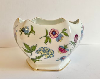 May include: A white porcelain bowl with a scalloped rim and a floral design. The bowl features a variety of flowers in shades of pink, blue, yellow, and green.