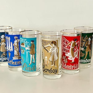 May include: A set of six clear glass tumblers with gold rims, each featuring a colorful graphic illustration of a city and its cultural icon. The glasses are labeled Hague, Athens, Paris, Bombay, Madrid, and London in stylized lettering.
