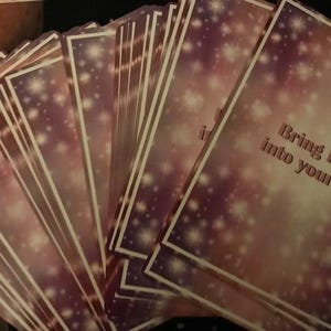 May include: A stack of cards with a pink and purple background and white glitter. The top card has the text "Bring light into your life".