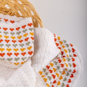 crochet baby heart blanket pattern with white yarn as base color in the middle with the shell stitch and autumn colors green orange and red for the hearts