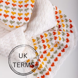 May include: A white crochet blanket with a border of orange, yellow, and green hearts. The blanket is folded in half, and the text "UK TERMS" is visible in the centre of the image.