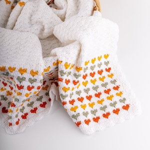 crochet baby heart blanket pattern with white yarn as base color in the middle with the shell stitch and autumn colors green orange and red for the hearts