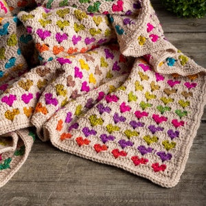 crochet heart blanket pattern with hearts in rainbow colors made with variegated yarn and beige yarn as the base color of the blanket.