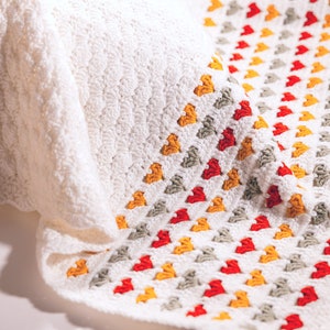 crochet baby heart blanket pattern with white yarn as base color in the middle with the shell stitch and autumn colors green orange and red for the hearts