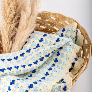 crochet heart blanket pattern made with yarn in shades of blue for the hearts and white as the base of the afghan. Shown folded in a wooden basket.