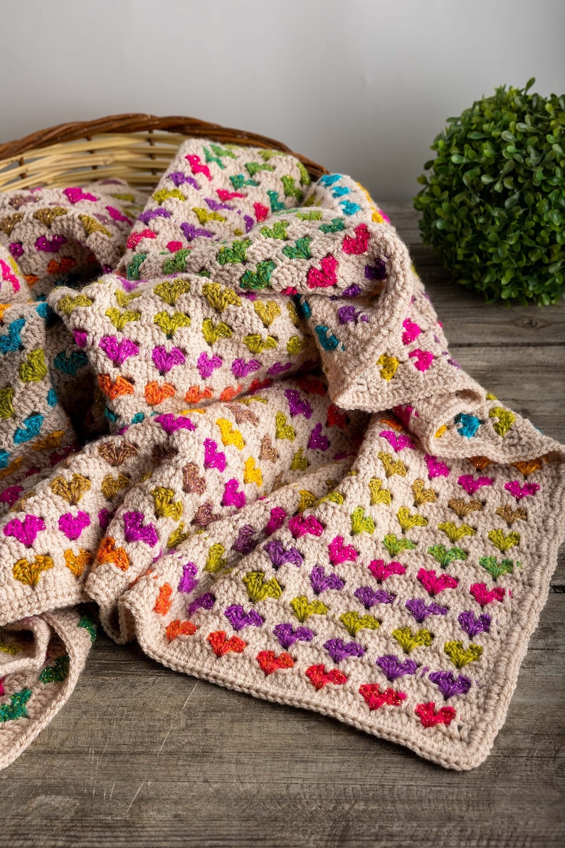 crochet heart blanket pattern with hearts in rainbow colors made with variegated yarn and beige yarn as the base color of the blanket.