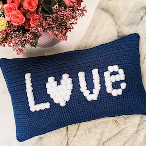 May include: A blue crocheted cushion with the word "LOVE" spelled out in white bobbles. The "O" is shaped like a heart.