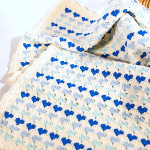 crochet heart blanket pattern made with yarn in shades of blue for the hearts and white as the base of the afghan. Shown folded in a woven basket.