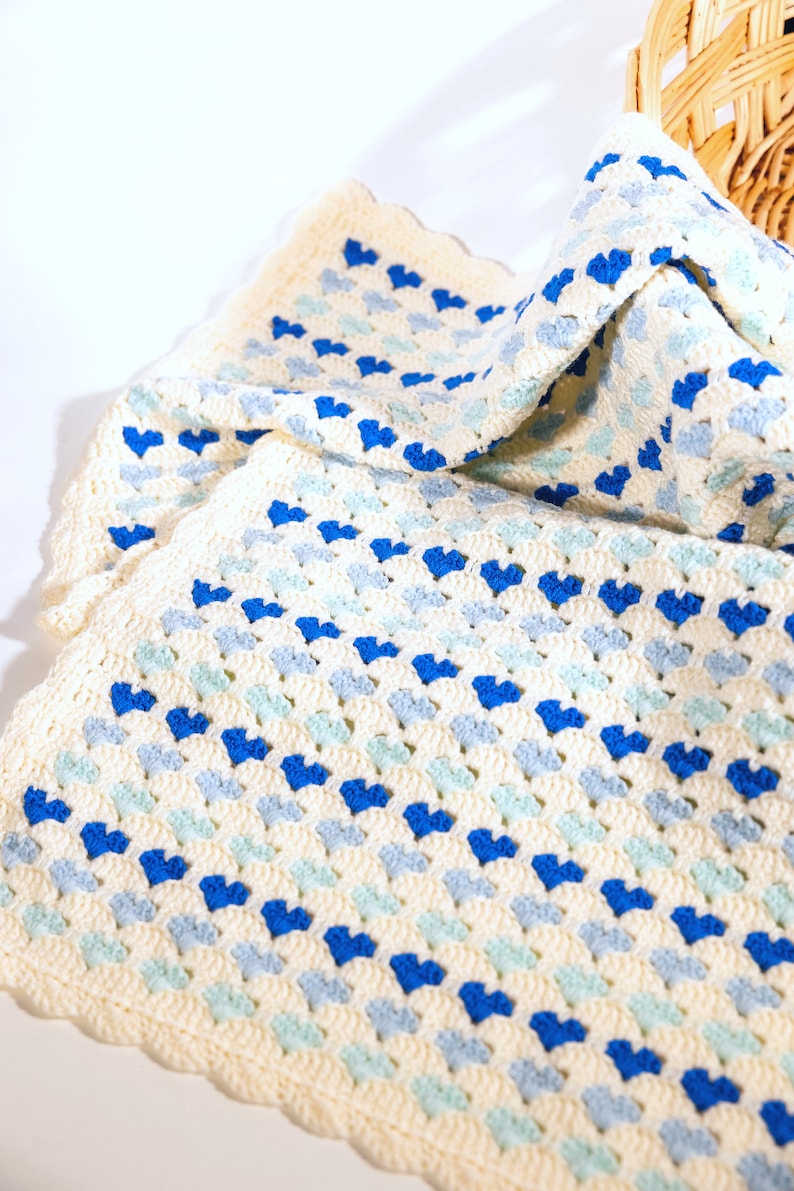 crochet heart blanket pattern made with yarn in shades of blue for the hearts and white as the base of the afghan. Shown folded in a woven basket.