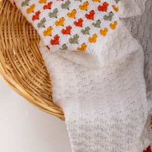 crochet baby heart blanket pattern with white yarn as base color in the middle with the shell stitch and autumn colors green orange and red for the hearts