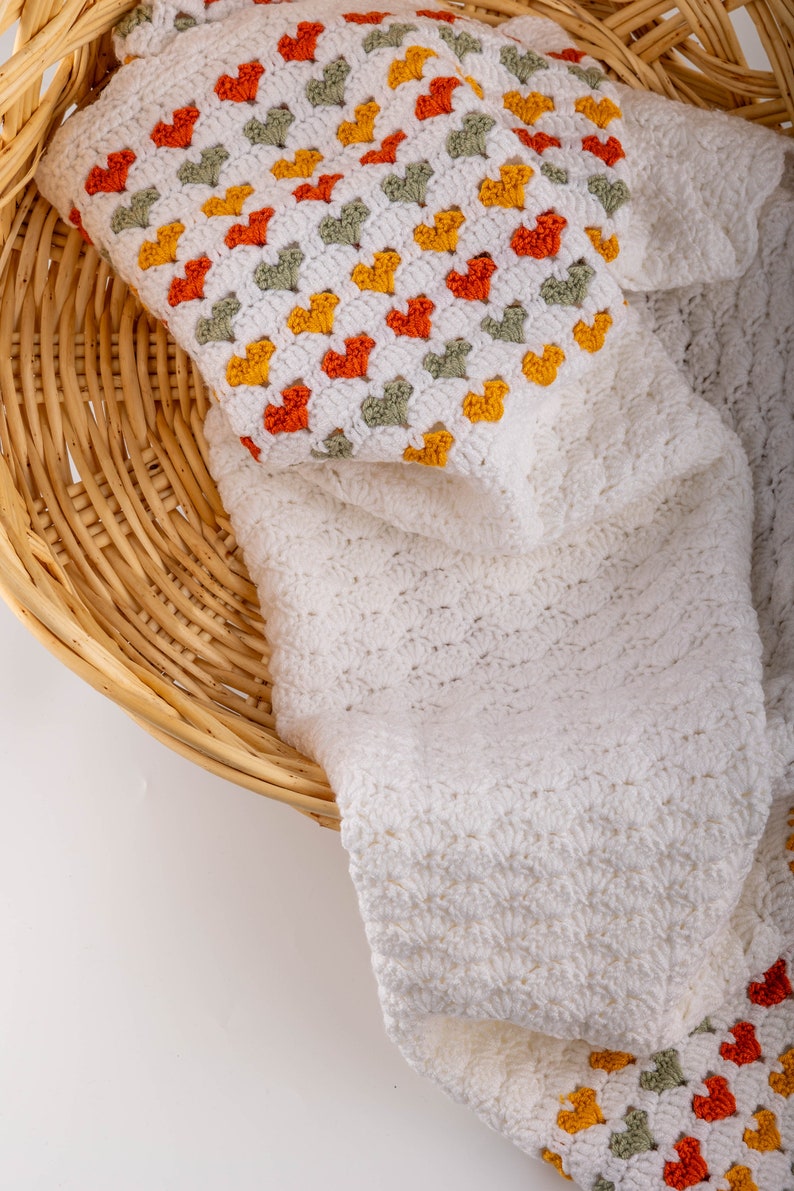 crochet baby heart blanket pattern with white yarn as base color in the middle with the shell stitch and autumn colors green orange and red for the hearts
