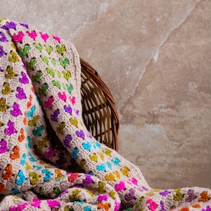 crochet heart blanket pattern with hearts in rainbow colors made with variegated yarn and beige yarn as the base color of the blanket.