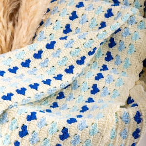 crochet heart blanket pattern made with yarn in shades of blue for the hearts and white as the base of the afghan. Shown folded in a wooden basket.