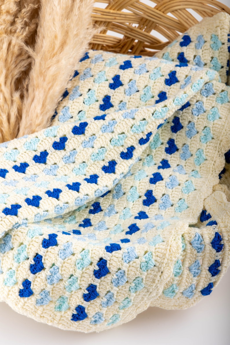 crochet heart blanket pattern made with yarn in shades of blue for the hearts and white as the base of the afghan. Shown folded in a wooden basket.